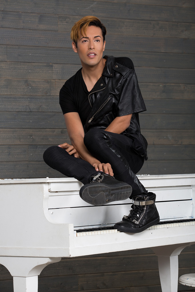 Dario in a black leather fold-over top, sitting on top of a white piano